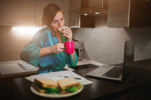 Donna impegnata a mangiare, bere caffè, parlare al telefono, lavorare su un laptop allo stesso tempo