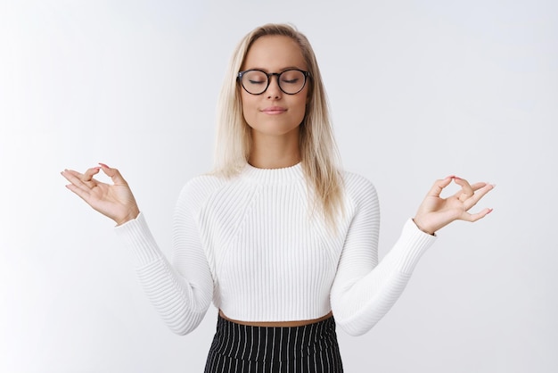 donna imprenditrice che fa una pausa meditazione per liberare la negatività e le cattive emozioni praticando yoga respirando profondamente con gli occhi chiusi e paziente sorriso rilassato in piedi nella posa del loto con gesto mudra