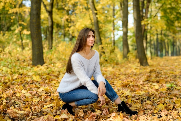 Donna in abbigliamento casual in posa nel parco con foglie gialle