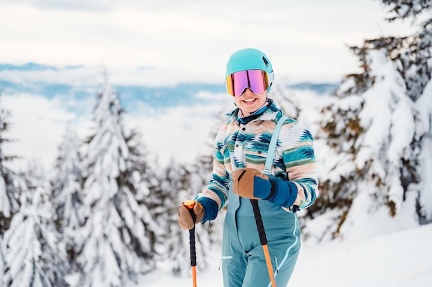Donna in abbigliamento da sci con casco e occhiali da sci in testa con bastoncini da sci Tempo invernale sulle piste In cima a una montagna e vista panoramica Sciatore alpino Sport invernali