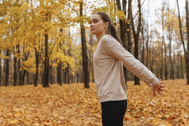 donna in abbigliamento sportivo che allunga le braccia dietro la schiena durante l'allenamento nel parco