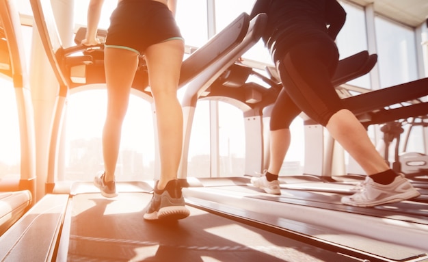 Donna in abbigliamento sportivo e scarpe da ginnastica in esecuzione su un tapis roulant in palestra contro la finestra