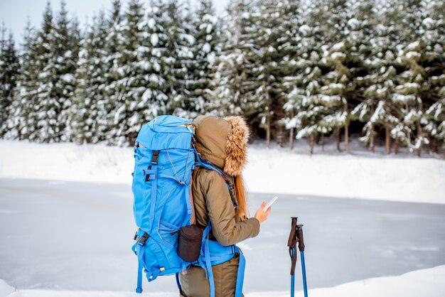 Donna in abiti invernali con zaino e bastoncini da tracciamento godendo di una splendida vista del paesaggio sulla foresta innevata e sul lago ghiacciato