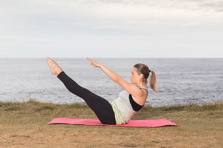Donna in abiti sportivi facendo pilates all'aperto su una stuoia rosa con il mare