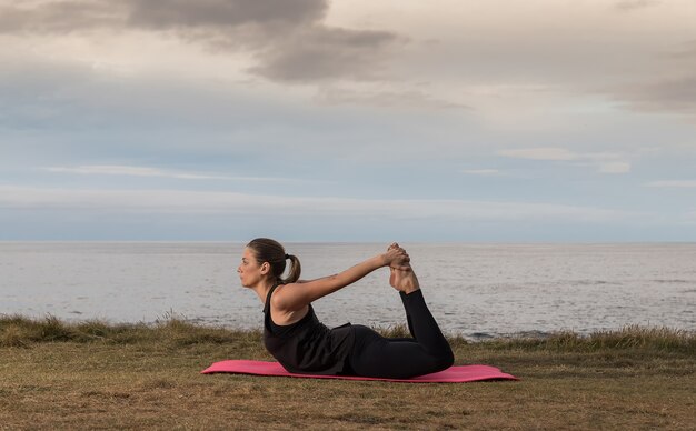 Donna in abiti sportivi facendo pilates all'aperto su una stuoia rosa con il mare