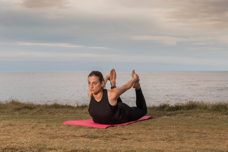 Donna in abiti sportivi neri che esercitano all'aperto su una stuoia rosa con il mare