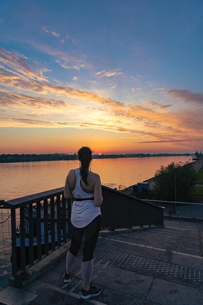 Donna in abiti sportivi sul ponte che guarda il tramonto mozzafiato sul fiume