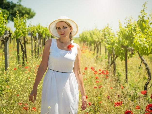 Donna in abito bianco e cappello nelle file dei campi di uva.