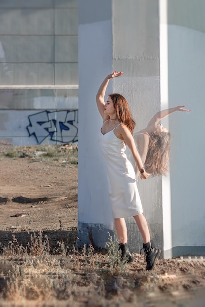 Donna in abito bianco e con i capelli lunghi in posa sotto il ponte sullo sfondo dei pilastri