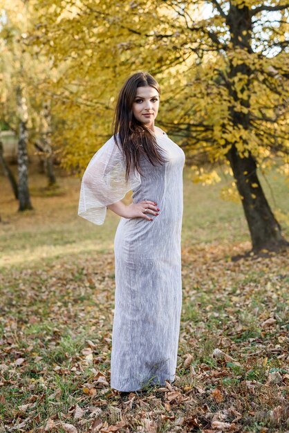 Donna in abito da sera elegante in posa nel parco d'autunno. Le luci del sole sugli alberi nei colori gialli