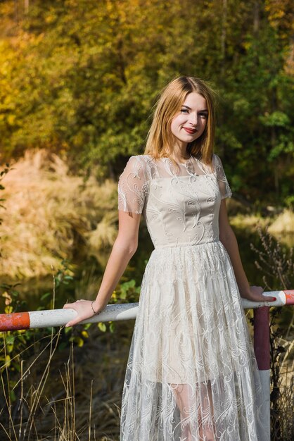 Donna in abito da sera elegante in posa nel parco d'autunno. Le luci del sole sugli alberi nei colori gialli