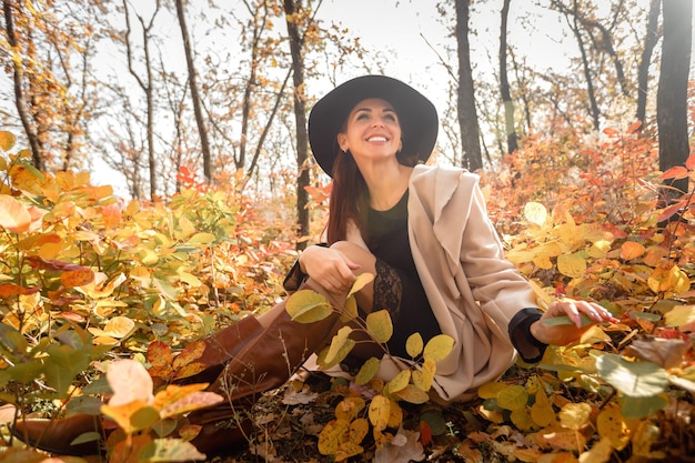 Donna in abito e cappello su sfondo di fogliame autunnale