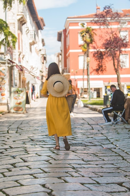 Donna in abito giallo con un po' di cappello di paglia che cammina per la vecchia città turistica in croazia