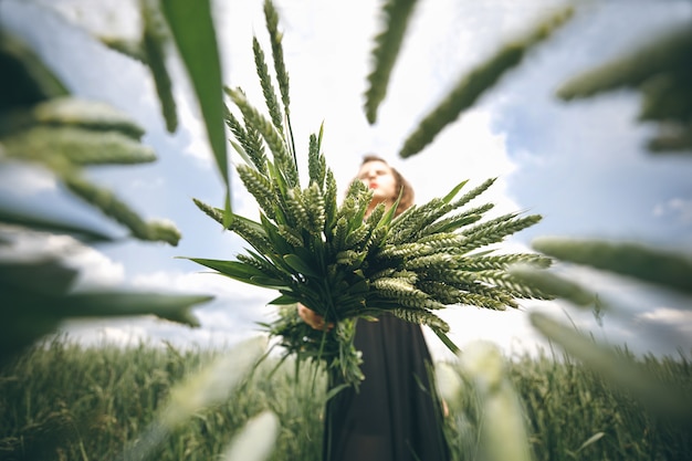 Donna in abito nero in piedi contro il cielo nuvoloso con bouquet di grano nelle mani