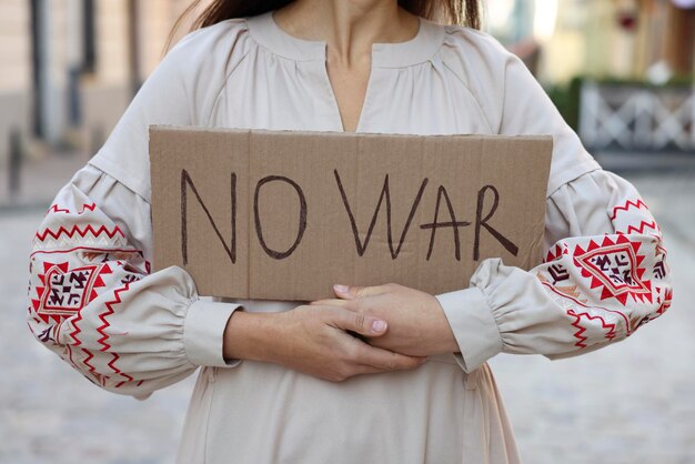Donna in abito ricamato tenendo poster No War all'aperto primo piano