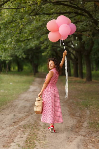 Donna in abito rosa con palloncini rosa e cesto di vimini nel parco verde domenica