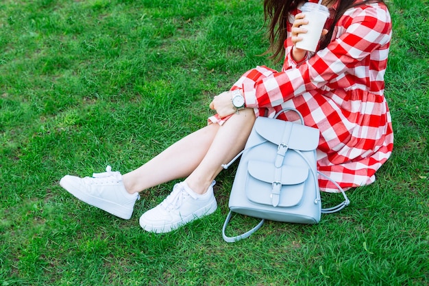 Donna in abito rosso che beve frullato mentre è seduta sull'erba verde nel parco