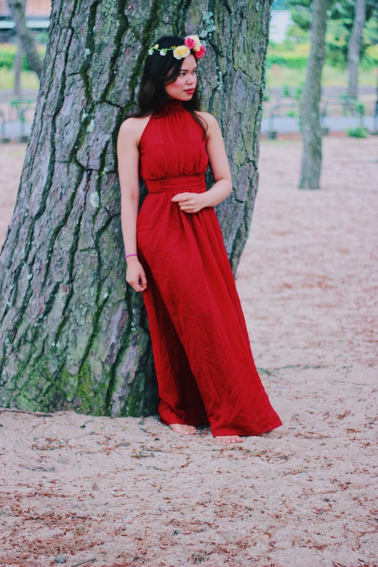 Foto donna in abito rosso in piedi contro il tronco dell'albero