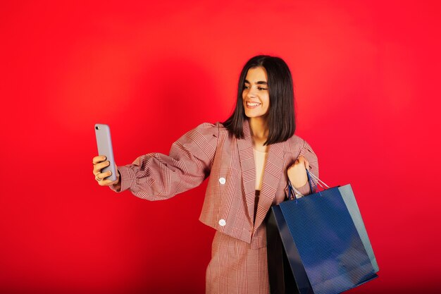 Donna in abito rosso prende un selfie sullo smartphone su una parete rossa