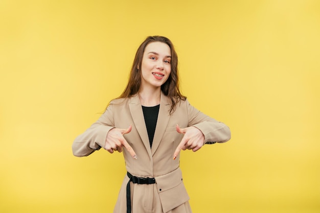 donna in abito si erge su uno sfondo giallo con un sorriso sul viso punta le dita verso il basso