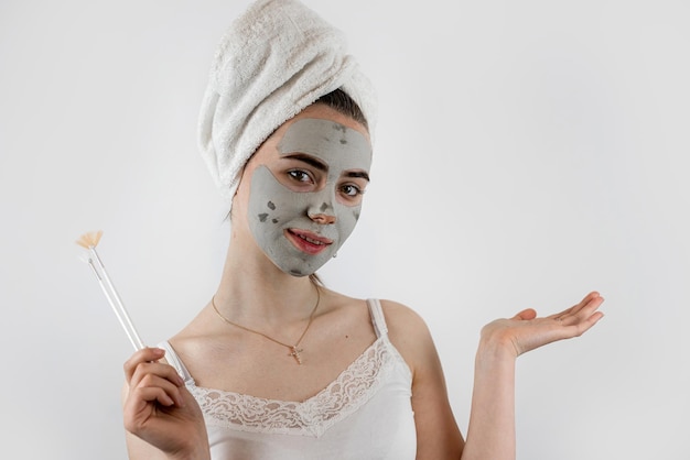 donna in asciugamano con pennello applicata una maschera pulente nera sul viso isolata su bianco maschera cosmetica come trattamento anti invecchiamento