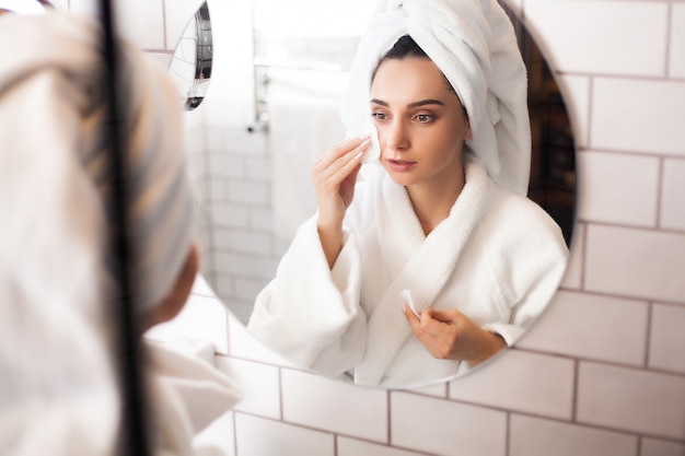 Donna in bagno con un asciugamano sulla testa si applica il trucco sul viso