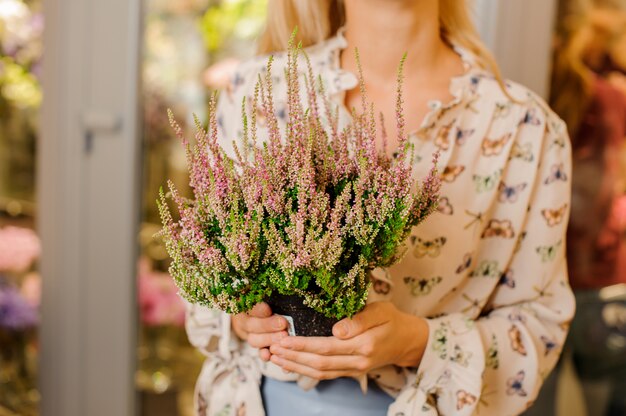 Donna in bella camicia che tiene un vaso con il fiore di fioritura
