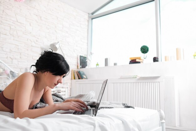 Donna in biancheria intima che digita sul computer portatile in camera da letto