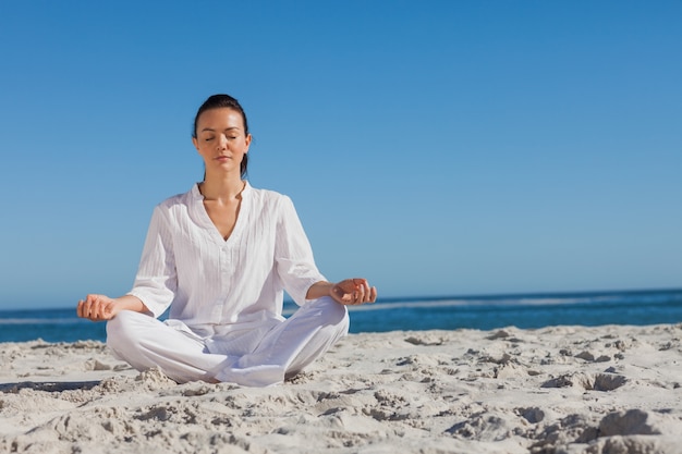 Donna in bianco facendo yoga sulla spiaggia