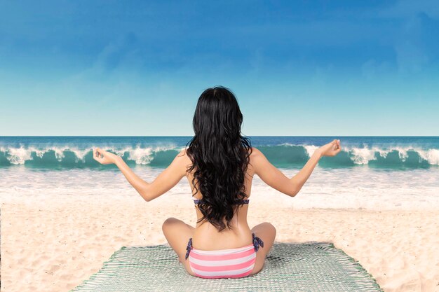 Donna in bikini che medita sulla spiaggia