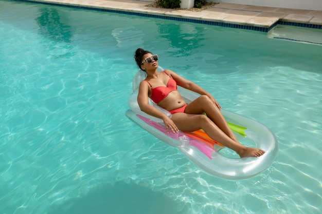 Donna in bikini che si rilassa su un tubo gonfiabile nella piscina nel cortile sul retro di casa