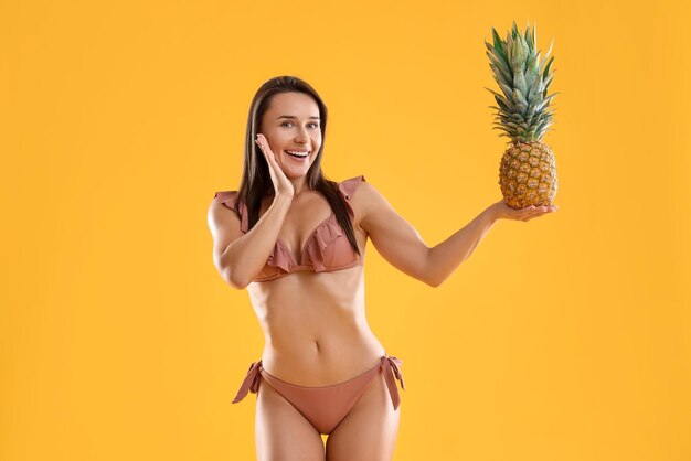 Donna in bikini elegante con ananas fresco su sfondo arancione