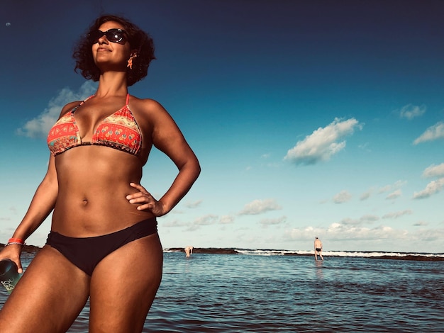Donna in bikini in piedi al mare contro il cielo