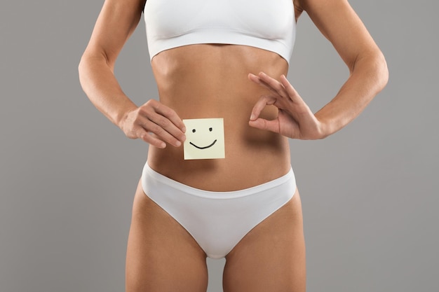 Donna in buona salute con corpo sottile in forma che tiene carta con faccina sorridente felice