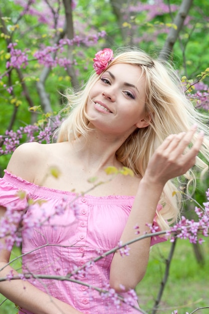 Donna in buona salute sorridente Hppy con capelli biondi di lusso in posa nel parco fiorito di sakura in fiore