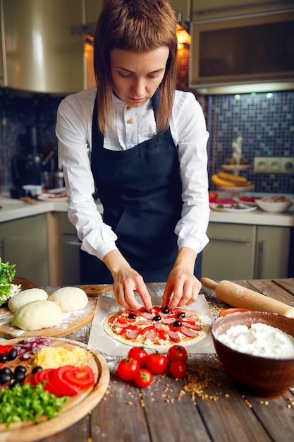 Donna in camicia bianca e grembiule che mette gli ingredienti sulla pizza