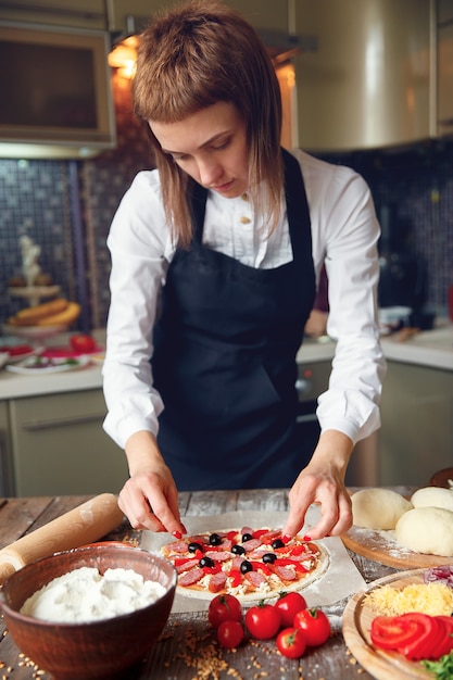 Donna in camicia bianca e grembiule mettendo gli ingredienti sulla pizza