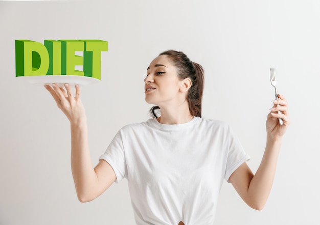 Donna in camicia con la gente isolata su bianco. Modello femminile che tiene un piatto con le lettere della parola Dieta. Scegliere un'alimentazione sana, una dieta, un'alimentazione biologica e uno stile di vita rispettoso della natura.