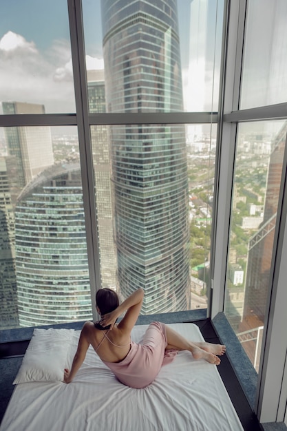 Donna in camicia da notte sdraiata sulla finestra del letto in un grattacielo vicino al letto