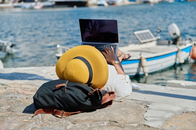 Donna in cappello che digita sul fondo della barca della baia dell'acqua del computer portatile