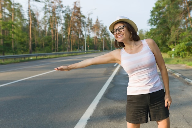 Donna in cappello che sta sulla strada che ferma automobile