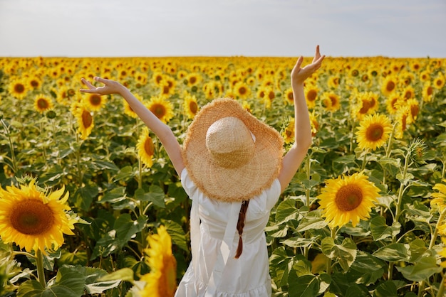 Donna in cappello con le mani alzate campo di girasoli natura estate