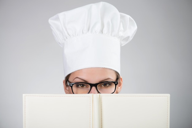 Donna in cappello da cuoco che guarda l'obbiettivo sopra il ricettario