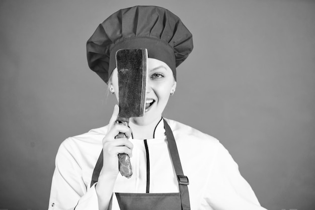 Donna in cappello da cuoco e grembiule macellaio tagliare carne donna felice cucinare cibo sano secondo ricetta chef professionista in cucina cucina casalinga con coltello da cucina chef tiene coltello cameriera professionista