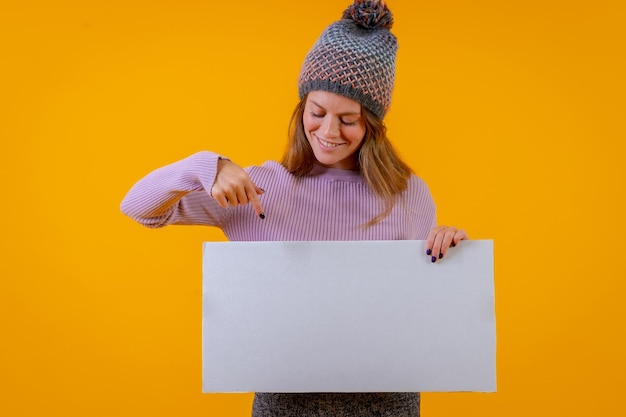 Donna in cappello di lana che punta a un cartello su un concetto di business sfondo giallo