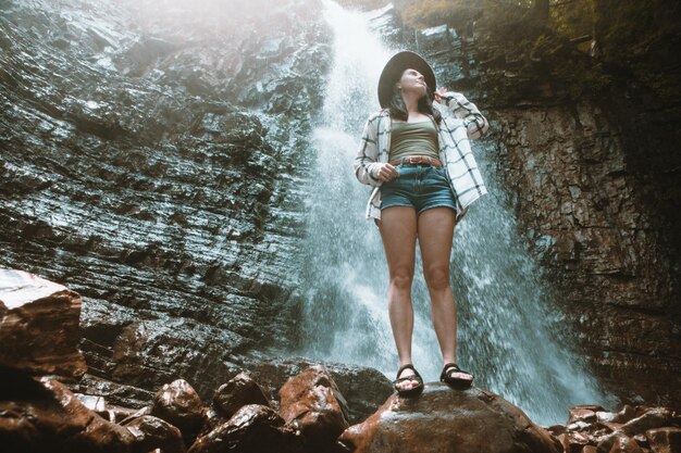 Donna in cappello marrone che gode della vista della cascata che fa un'escursione il concetto di viaggio