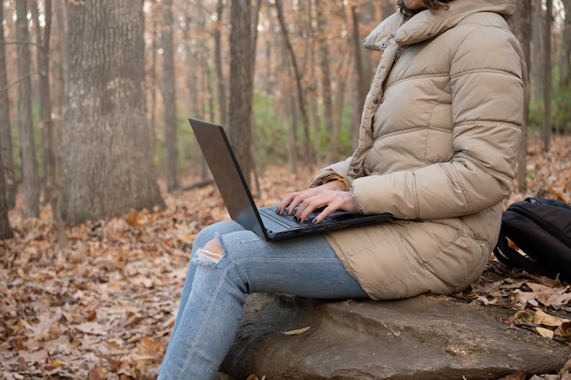 Donna in cappotto che lavora con il computer portatile nella foresta, con spazio di copia