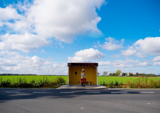 Donna in cappotto con valigia alla fermata dell'autobus di campagna