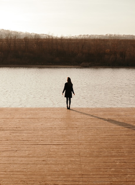 Donna in cappotto nero, godersi il tramonto vicino al fiume