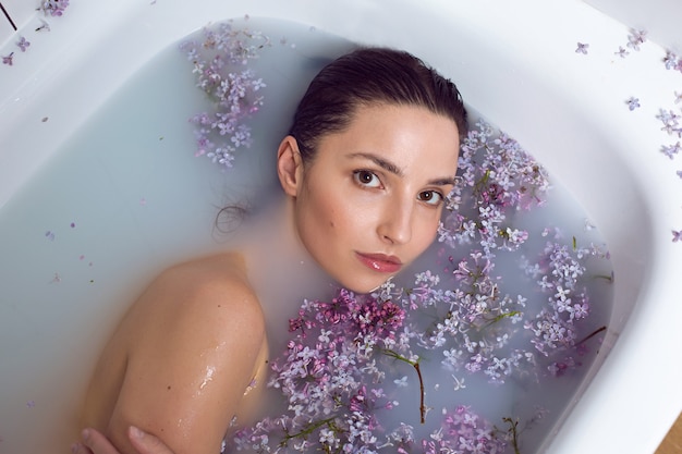 donna in costume da bagno facendo il bagno con latte e fiori lilla